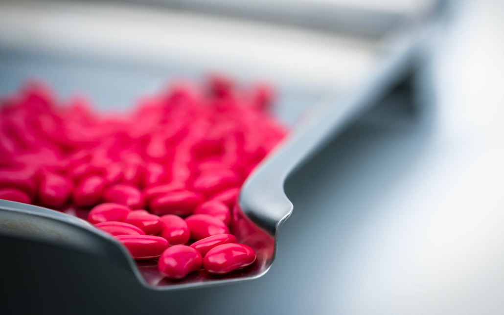 Coated red tablet on a metal chute